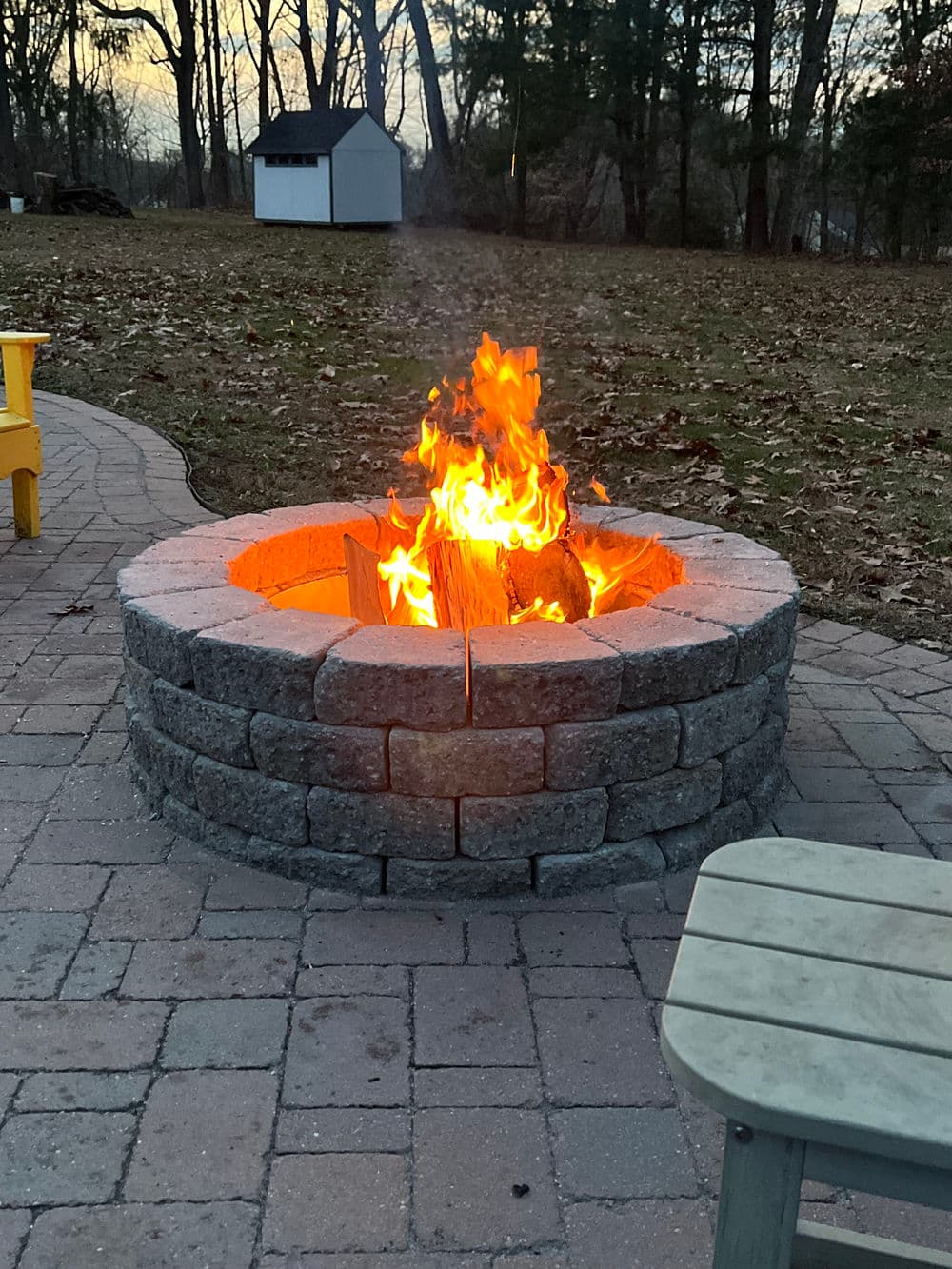 Cozy fire pit with flames and stacked logs in a backyard setting during sunset.