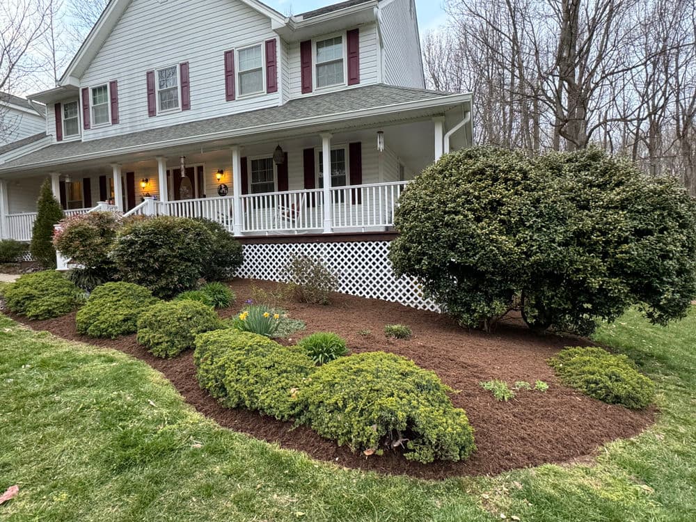 Front yard landscaping featuring shrubs, mulch beds, and a white porch on a two-story home.